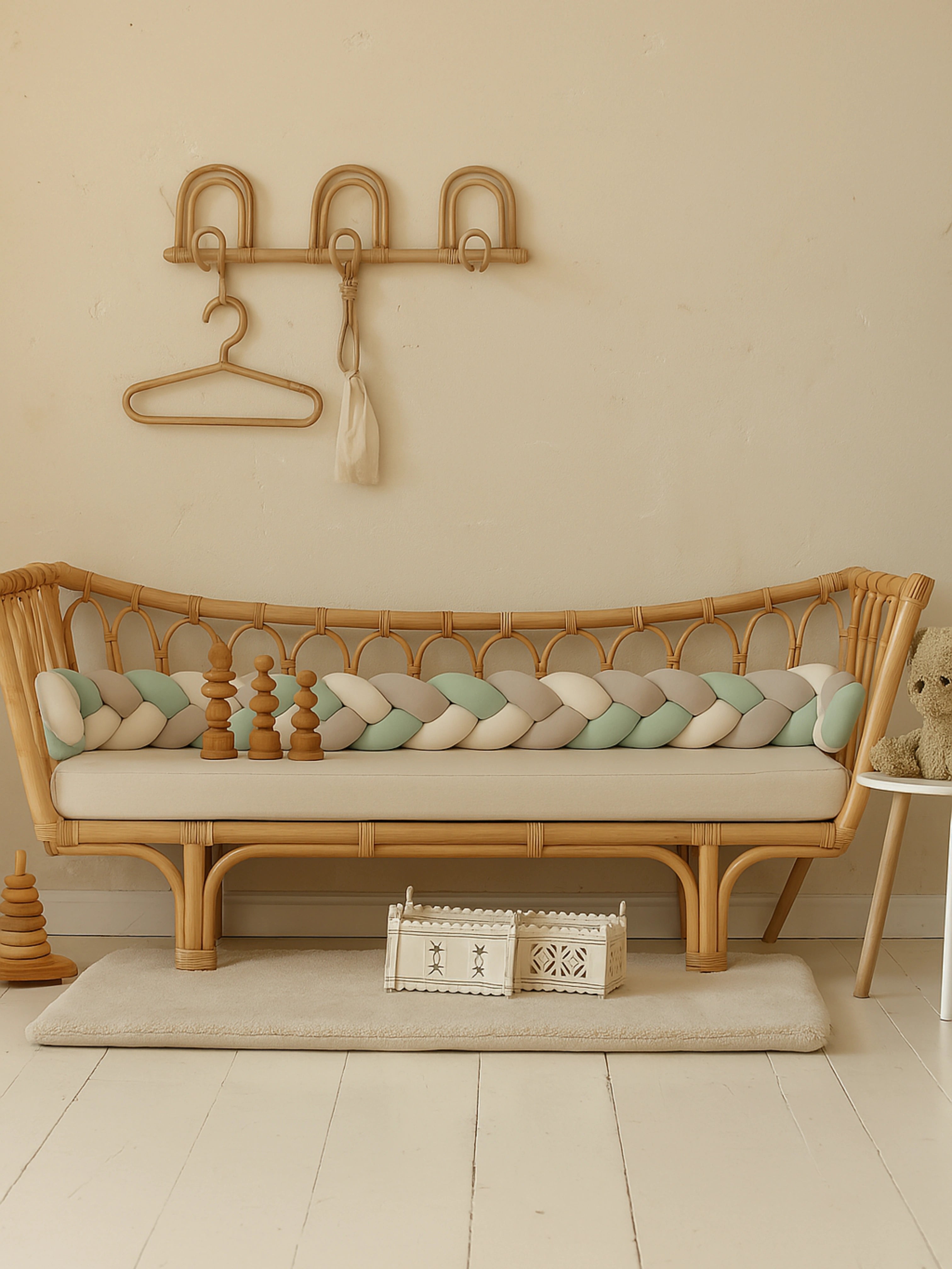 Tresse de lit bébé vert d’eau, beige et blanc sur un canapé en rotin, décor minimaliste et ambiance naturelle pour chambre enfant
